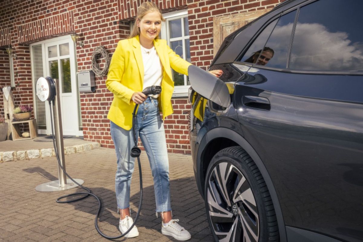 Person steht mit einem Ladekabel neben einem E-Auto