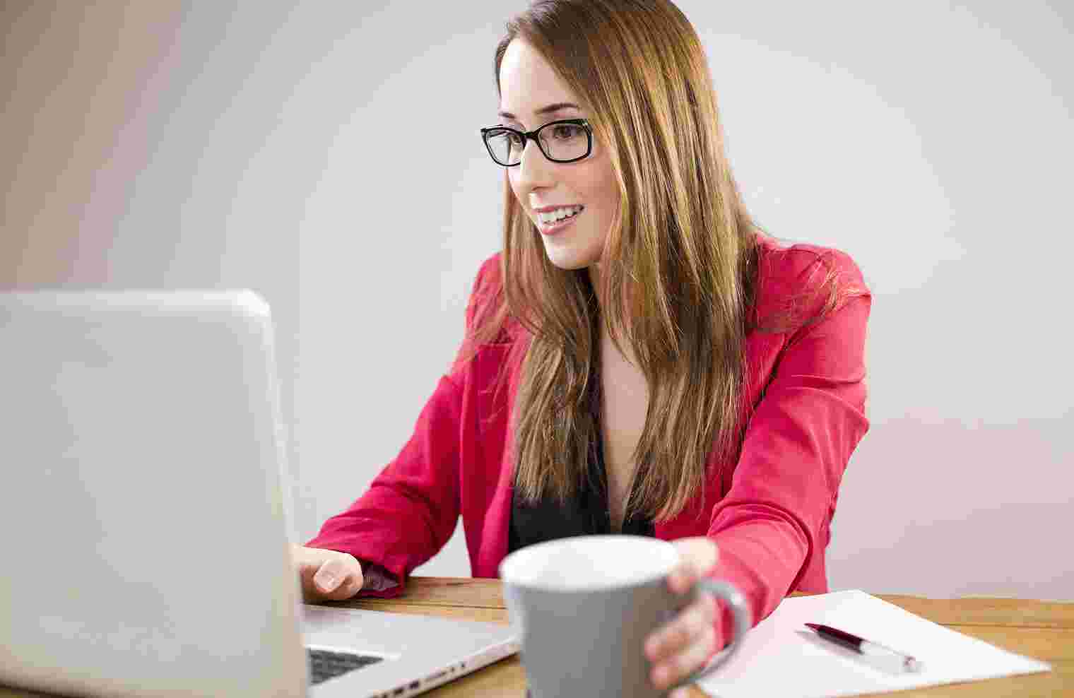 Frau sitzt an einem Laptop mit Tasse in der Hand
